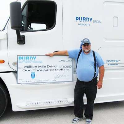 Purdy Bros truck driver standing on the side of truck with a $1,000 check in his hand